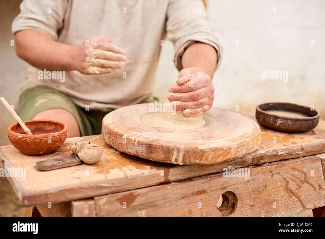 Potter maschio maestro in camicia di lino leggero con pentola di argilla bagnata in mano. Le mani dell'uomo hobby di ceramica scolpiscono in argilla Foto Stock
