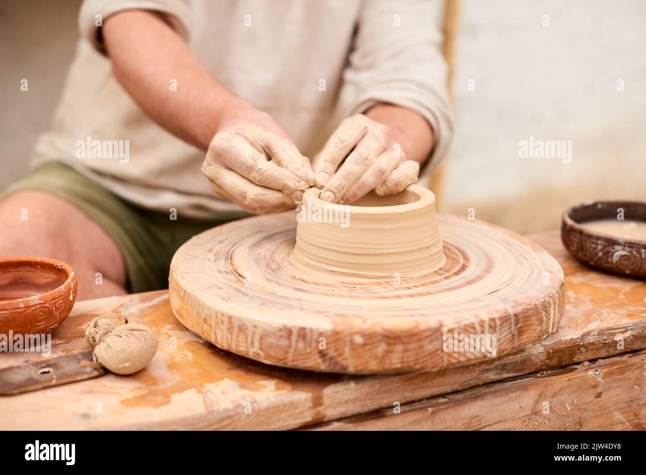 maestro artigiano maschile in camicia di lino chiaro scolpisce caraffa, ciotola o vaso di argilla Foto Stock