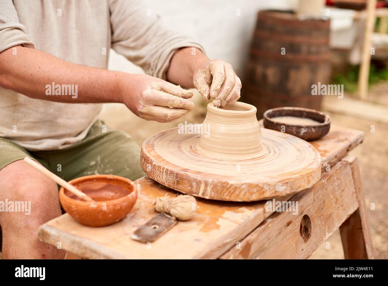 maestro artigiano maschile in camicia di lino chiaro scolpisce caraffa, ciotola o vaso di argilla in villaggio Foto Stock