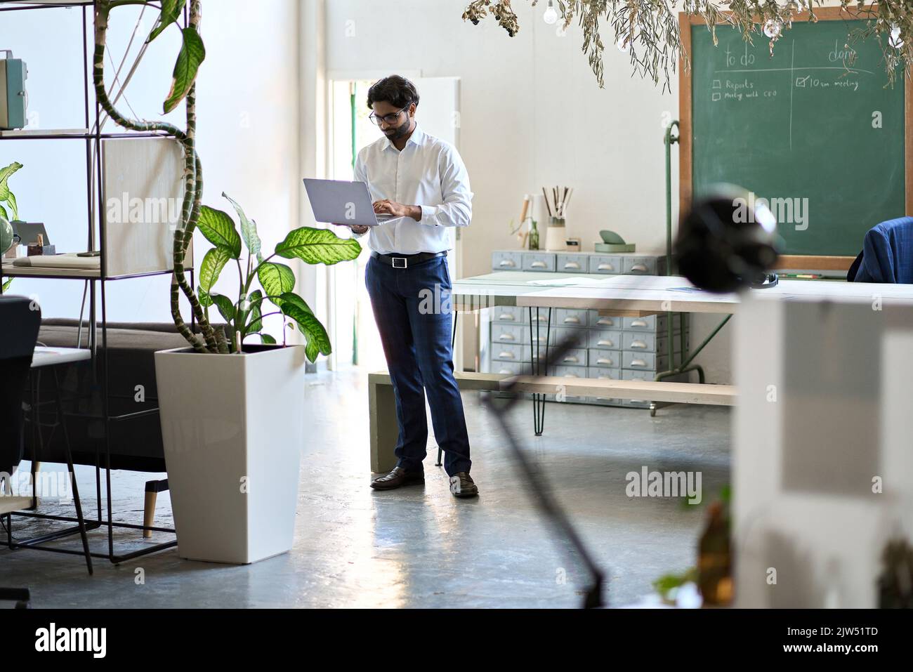 Giovane uomo d'affari indiano manager che lavora su un computer portatile in piedi in ufficio. Foto Stock