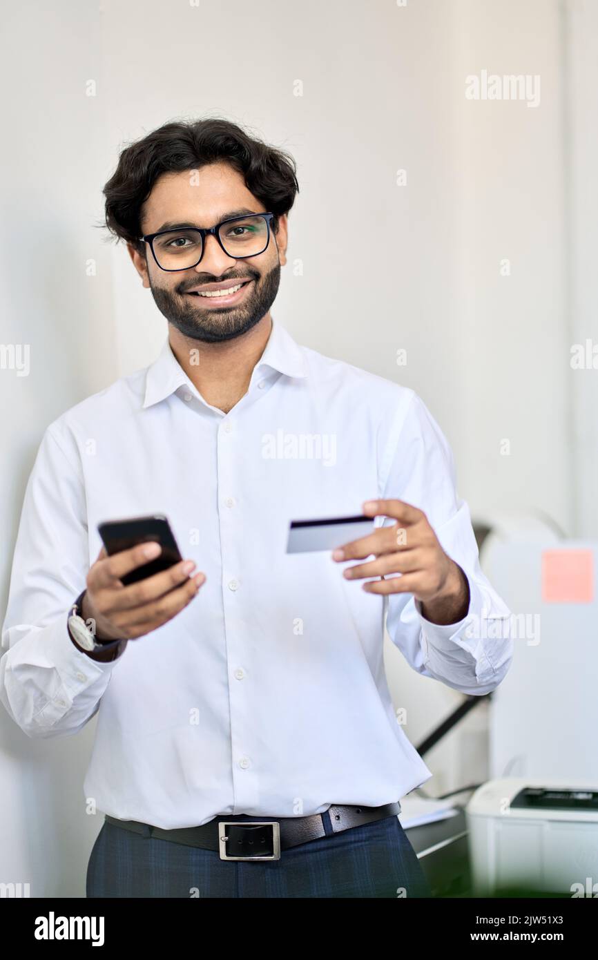 Uomo d'affari indiano sorridente usando il telefono che tiene la carta di credito che fa il pagamento del e. Foto Stock