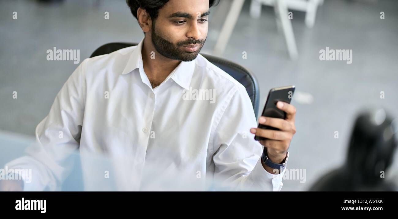 Uomo indiano occupato di affari che usa il telefono delle cellule al posto di lavoro in ufficio. Foto Stock