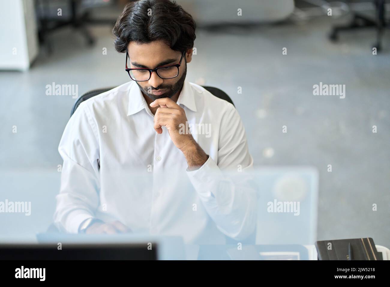 Uomo d'affari indiano serio occupato che analizza i dati di mercato, guardando il computer. Foto Stock