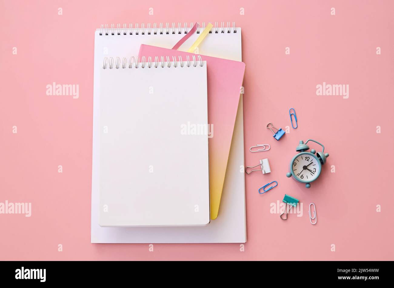 Piccola sveglia e forniture scolastiche su sfondo rosa, piatto, vista dall'alto. Foto Stock