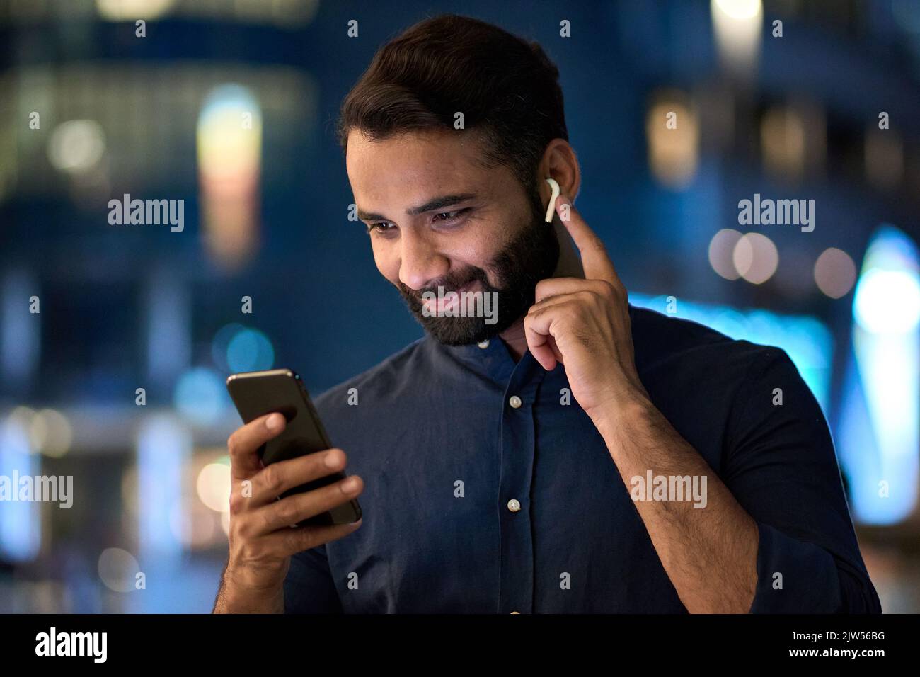 Un uomo indiano che indossa un auricolare con videochiamata sul telefono cellulare all'aperto. Foto Stock