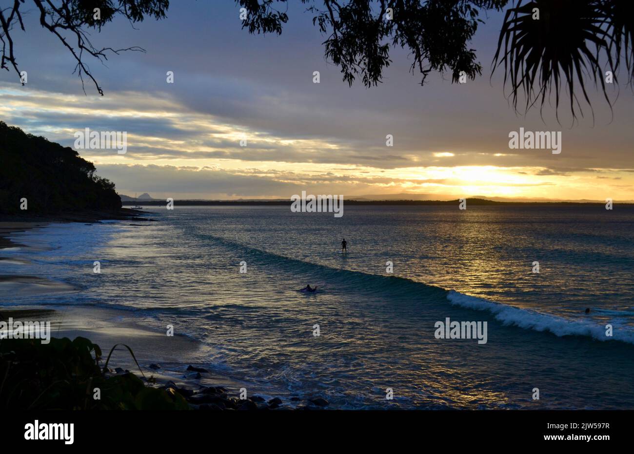 Surfista e paddleboard immergiti nell'ultimo momento del tramonto e della luce del crepuscolo sulla spiaggia e sulle onde dell'oceano a Granite Bay nel Parco Nazionale di Noosa Heads Foto Stock