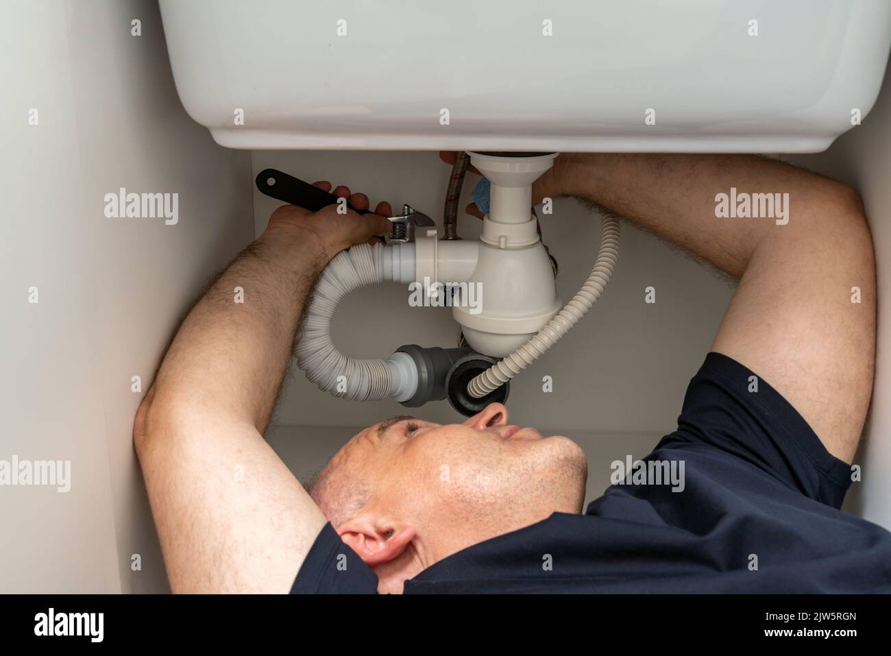 Primo piano di un uomo in una posizione difficile cercando di fissare il tubo sotto il lavandino Foto Stock