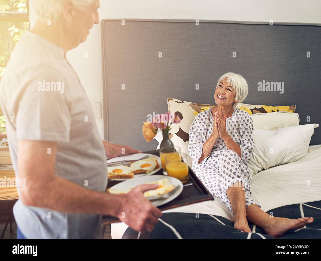 Egli sa ancora come spazzarla via dai piedi. Un uomo anziano che porta sua moglie colazione a letto. Foto Stock
