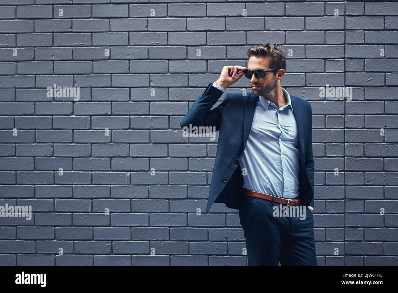 Il successo non va mai fuori di stile. Un bel giovane uomo d'affari che si trova contro una parete grigia di mattoni di facciata. Foto Stock