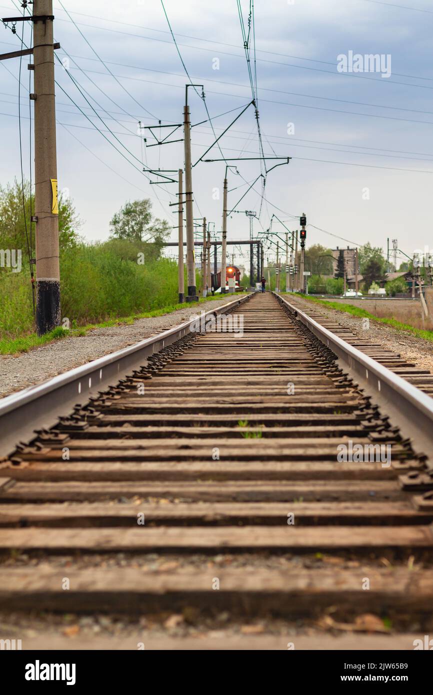 Il semaforo rosso è acceso. Uomo in lontananza cammina lungo binari ferroviari verso il treno. Sfondo astratto sfocato delle ferrovie in serata. Foto Stock