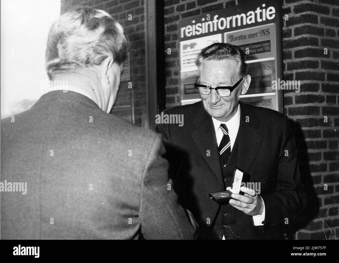 Immagine della consegna di una medaglia d'argento alle gambe da parte di ir. J.A. Muetstege (a destra, capo dell'agenzia distrettuale Noord-Oost dell'N.S.) al sindaco E. Talstra van Dantumadeel durante l'apertura del nuovo edificio della stazione N.S. di Veenwouden a Veenwouden. Foto Stock