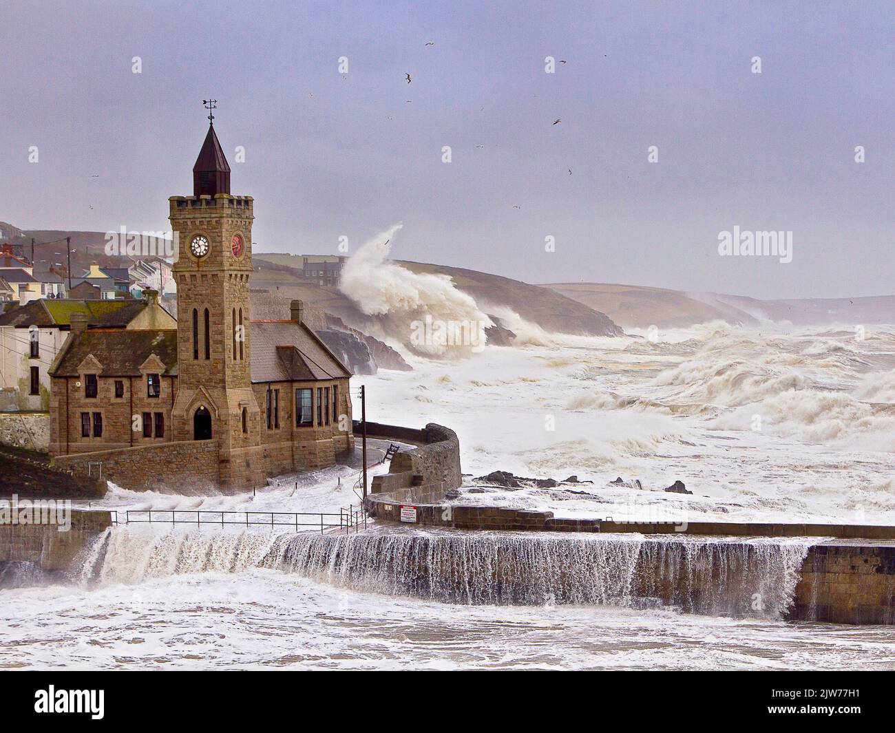2014 tempesta che colpisce la torre dell'orologio dell'Istituto Porthleven. Enormi onde che si infrangono sulle scogliere dietro. Foto Stock