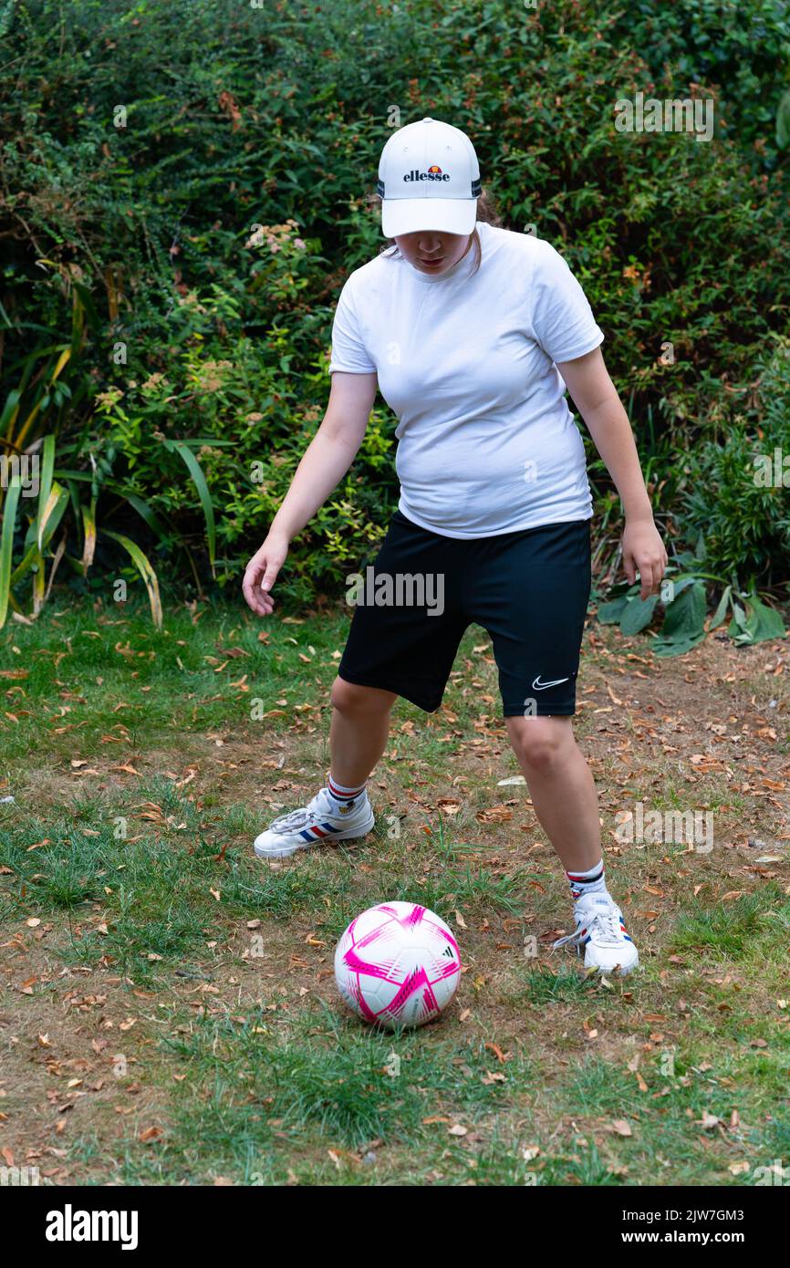 Donna con berretto Ellesse e pantaloncini Nike che praticano abilità calcistiche in parco Foto Stock