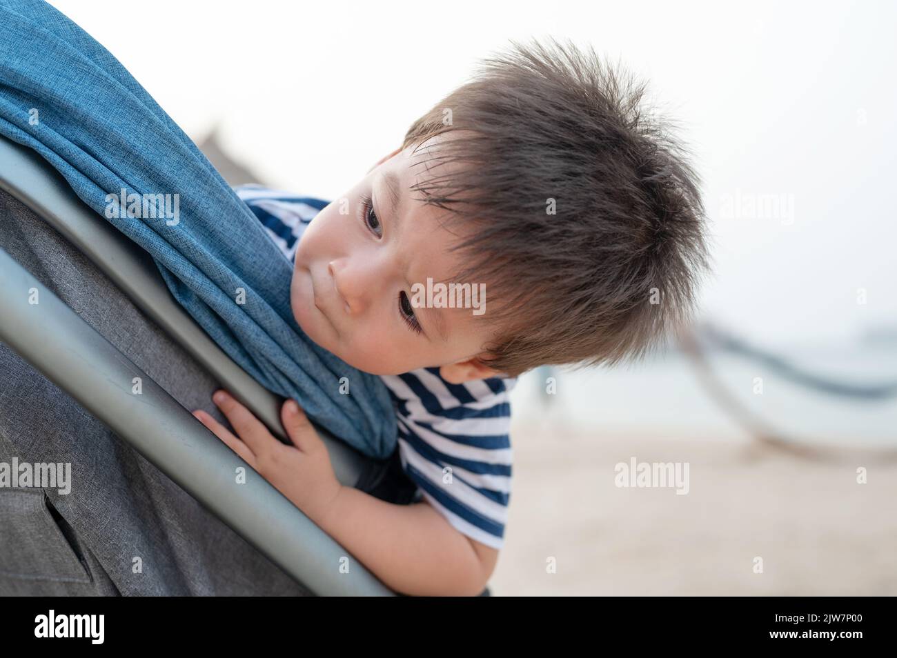 Bambino seduto nel passeggino sulla spiaggia in riva al mare durante le vacanze estive Foto Stock