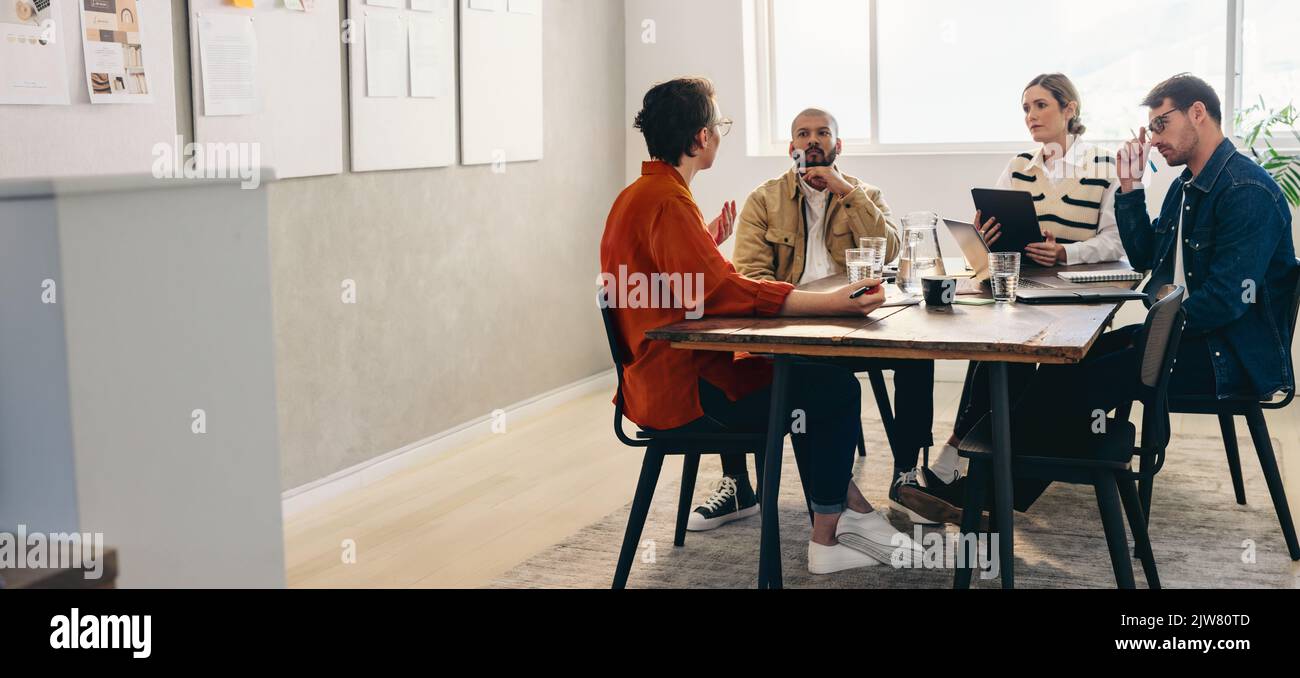 Gruppo di imprenditori creativi che hanno una discussione durante una riunione in un ufficio. Progettisti diversi che condividono idee mentre lavorano insieme su una nuova de Foto Stock