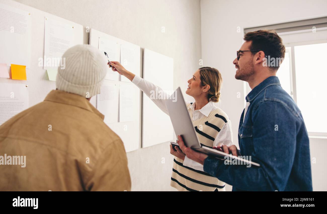 Brainstorming in un ufficio creativo. Gruppo di imprenditori diversi che discutono alcuni rapporti di marketing su una bacheca. Il team aziendale creativo è sempre più partecipe Foto Stock