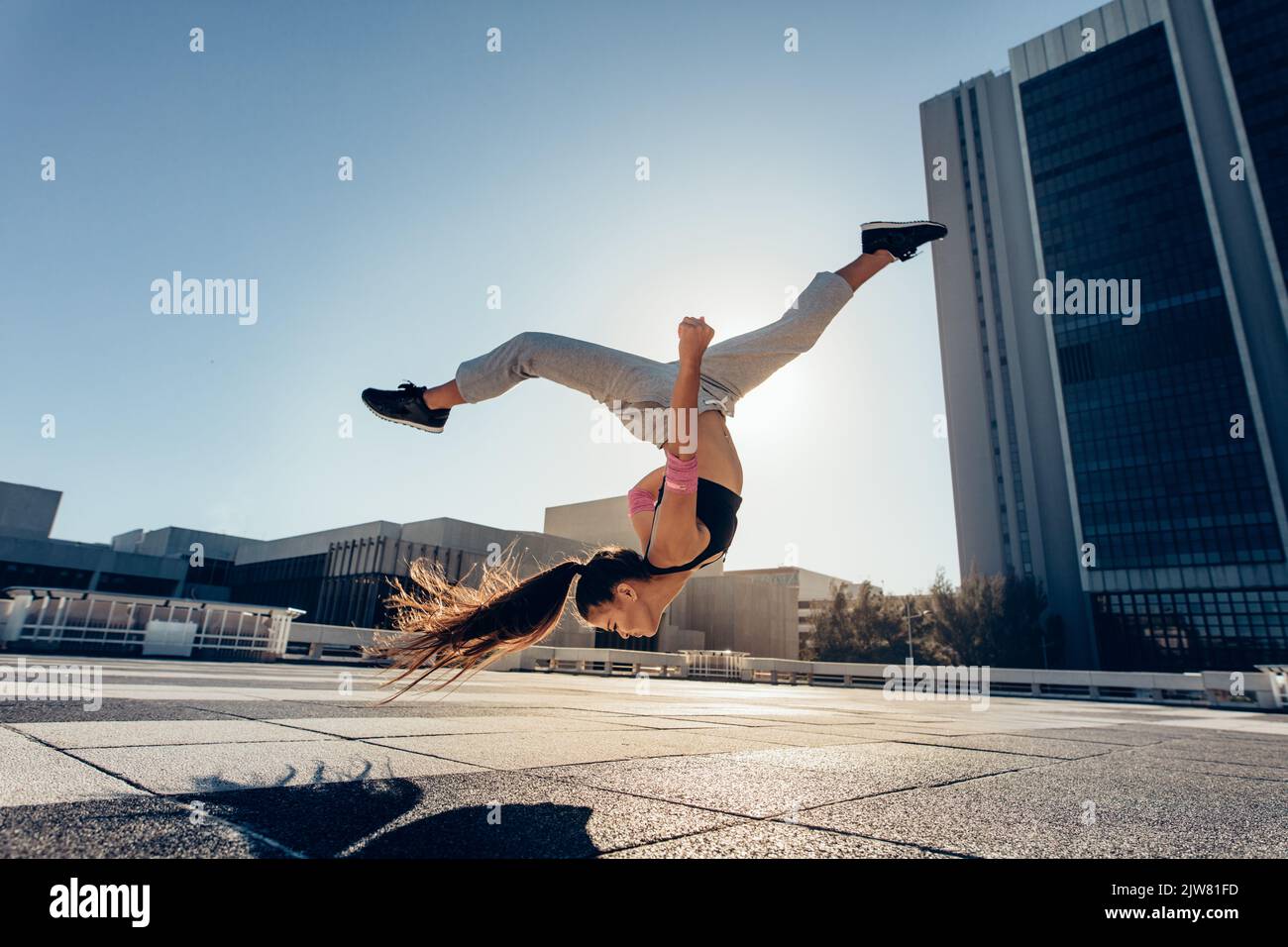 Un giovane sportivo che si esibisce in un'ambientazione all'aperto in città. Atleta femminile che pratica il tricking contro uno sfondo urbano. Foto Stock