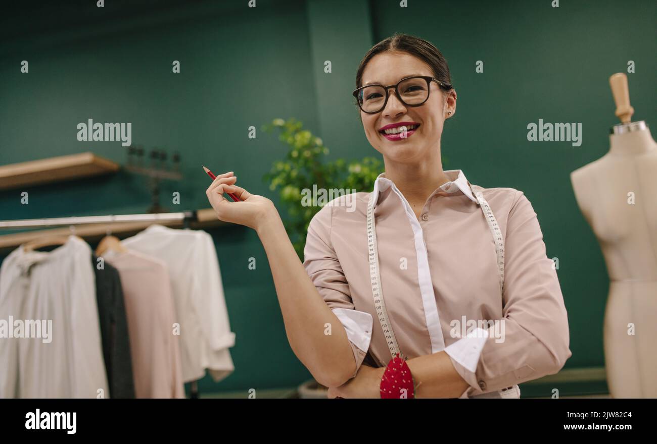 Bella giovane comò in piedi in officina e sorridente. Felice attraente stilista di moda in piedi nel suo studio creativo. Foto Stock
