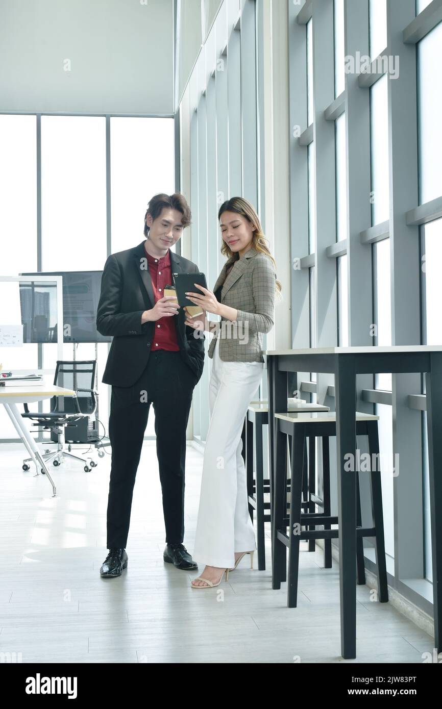 Felice uomo e donna asiatico busimess guardando il telefono cellulare per rilassarsi dopo il lavoro in ufficio Foto Stock