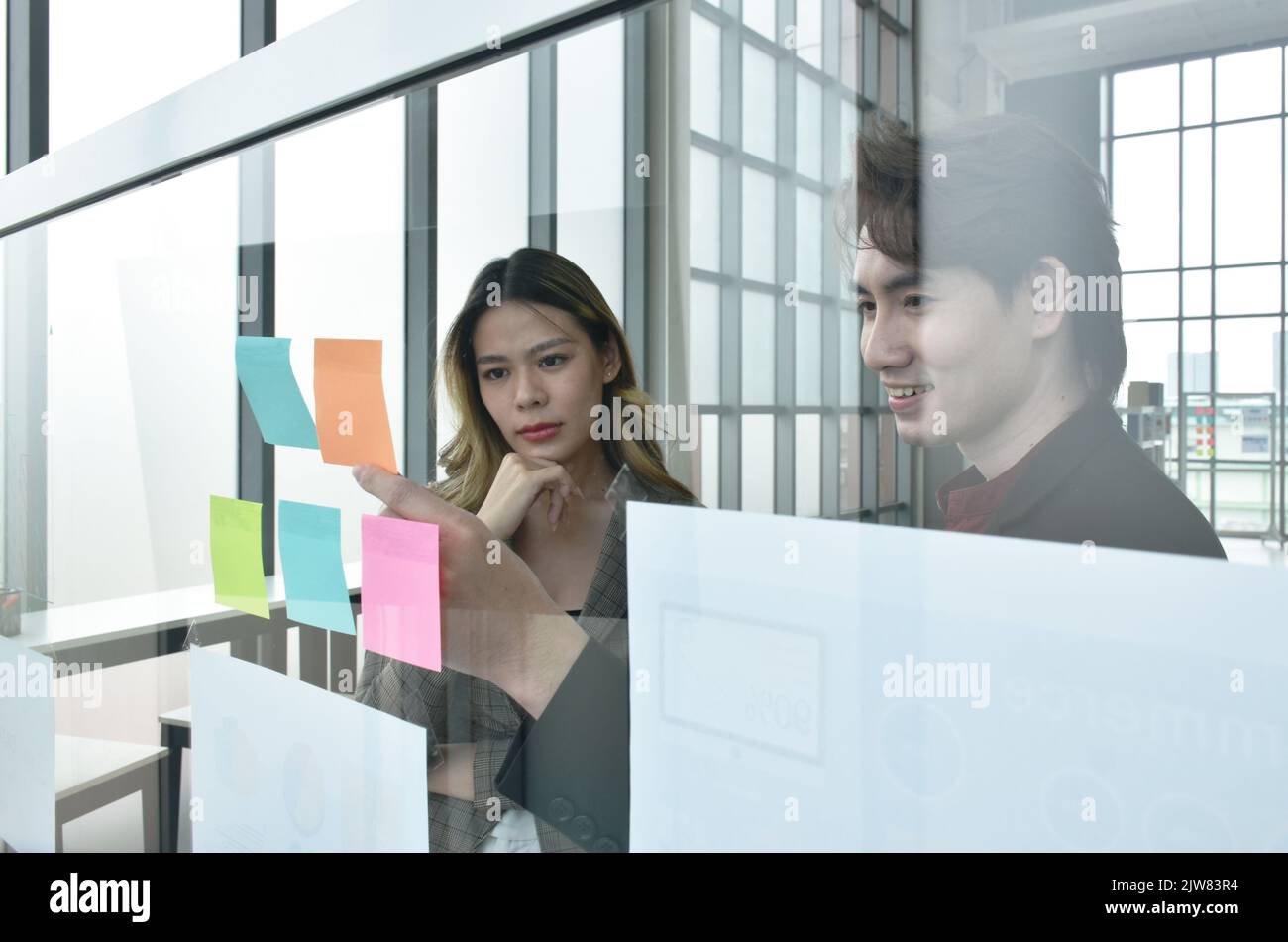 Uomo e donna asiatico di affari che guardano il bastone della nota della carta sul bordo di vetro per discutere e lavorare nell'ufficio Foto Stock