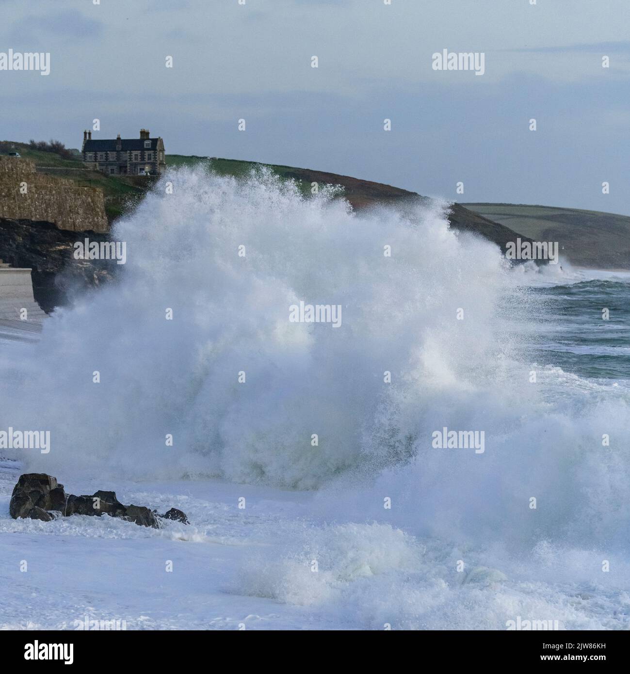 Onde massicce che battono sulla spiaggia di Porthleven con Tye Rock Manor appollaiato sulla scogliera dietro. Foto Stock