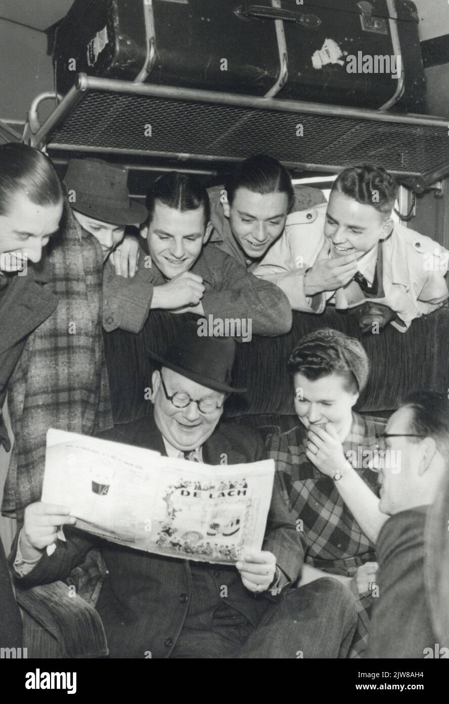 Immagine di un certo numero di persone intorno ad un uomo con una rivista di scherzo in un compartimento del treno (foto pubblicitaria). Foto Stock