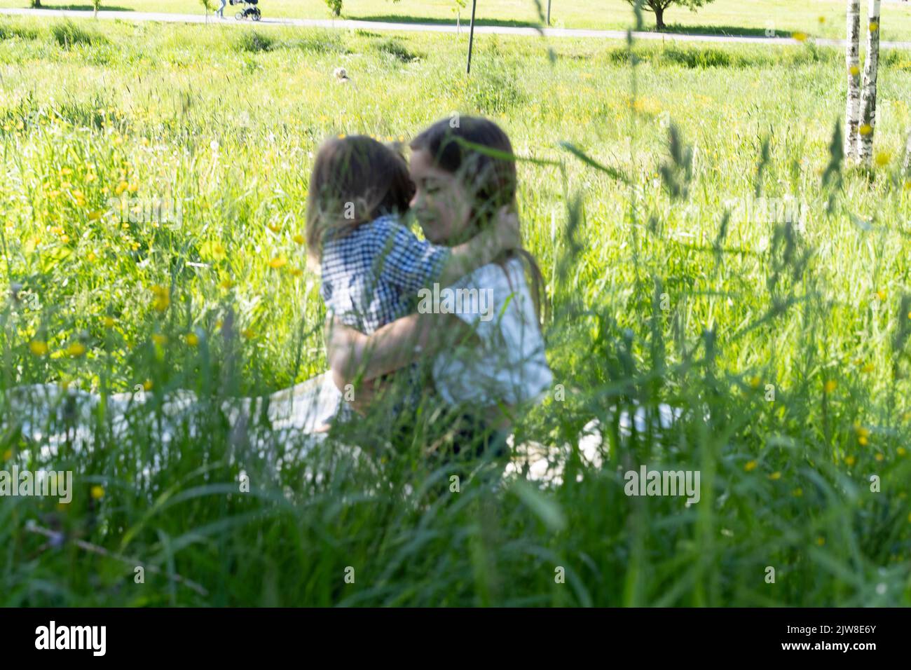 Fratello e sorella giocano nel parco tra l'erba verde. I bambini abbracciano strettamente. Picnic fuori città. Infanzia. Relazioni. Foto Stock