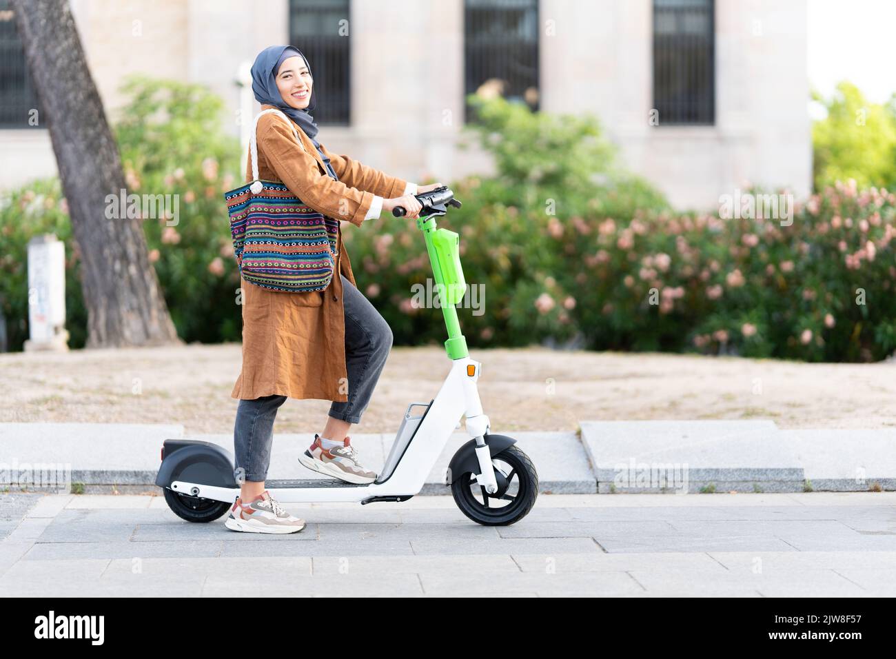 Donna musulmana in posa mentre usa uno scooter elettrico Foto Stock