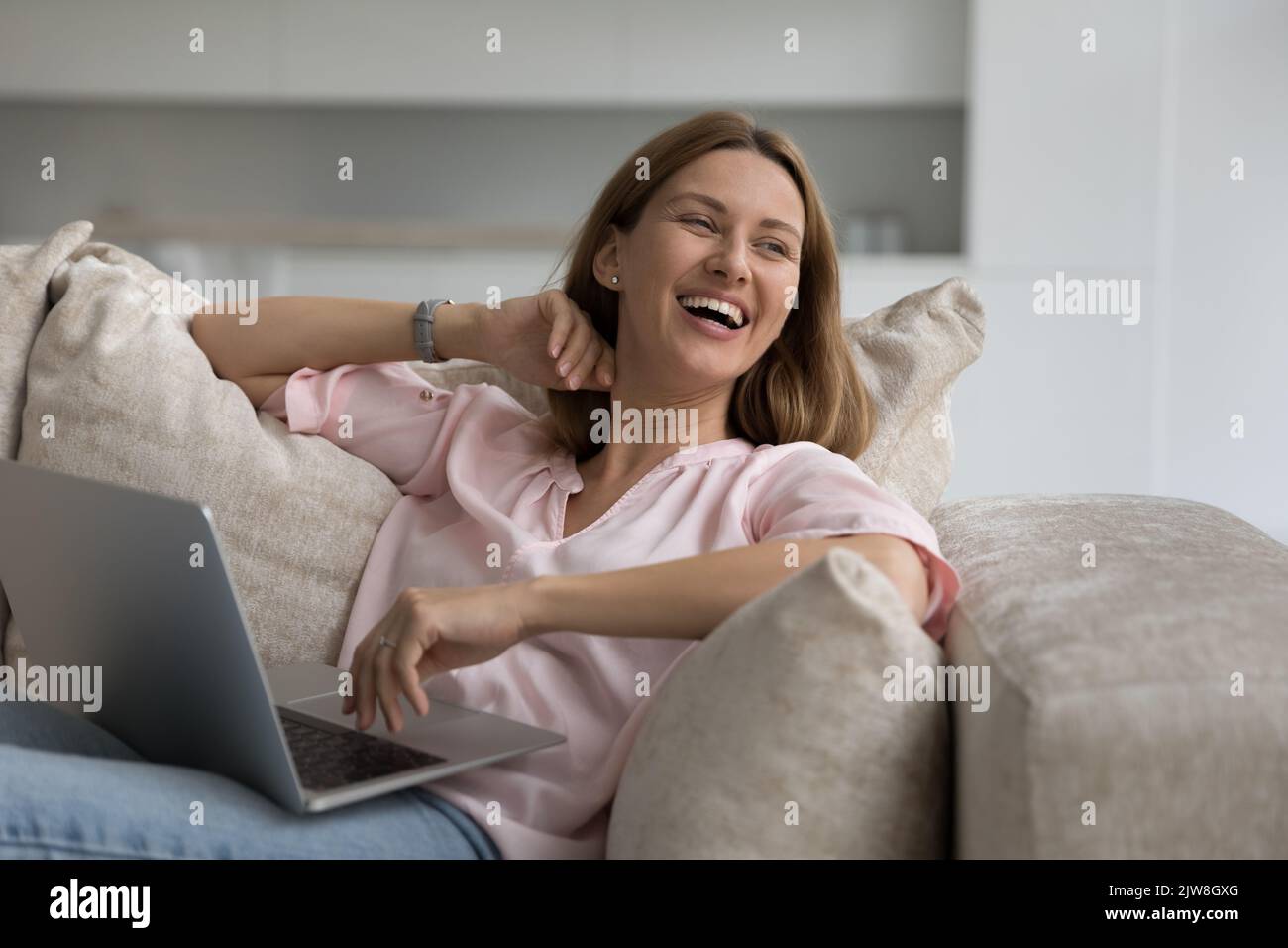 Allegra donna freelance che lavora sul divano di casa, tenendo il laptop Foto Stock