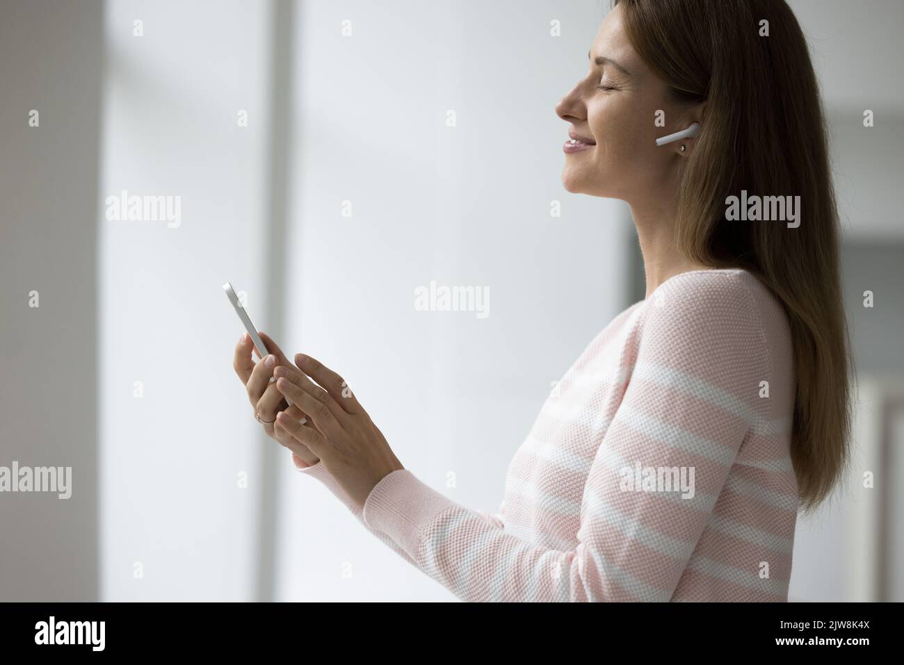 Donna allegra e tranquilla con cuffie wireless all'orecchio Foto Stock