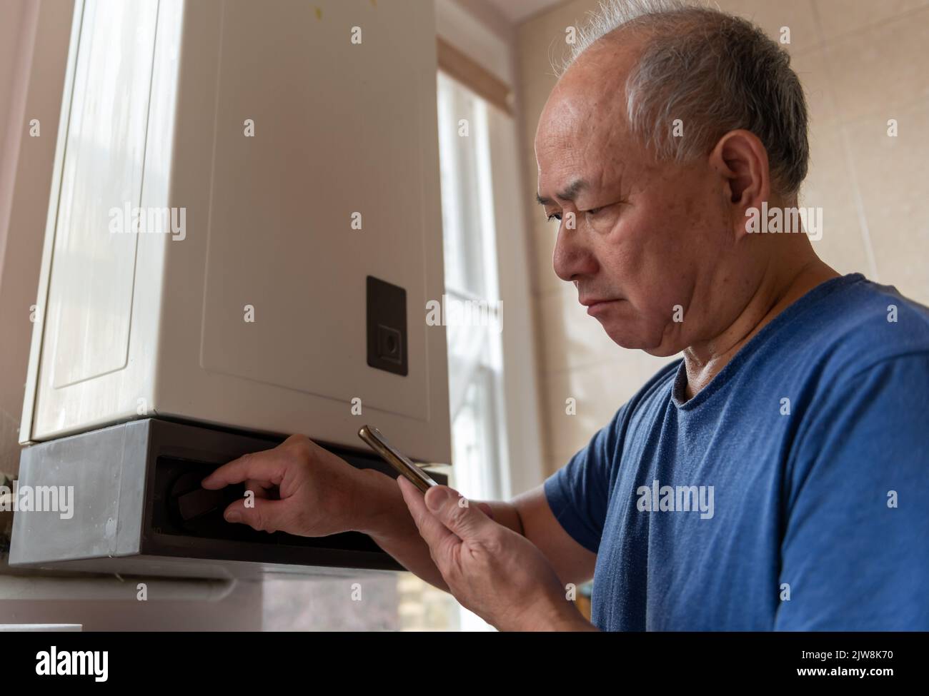 Un uomo anziano che abbaglia la caldaia dell'acqua calda per risparmiare denaro cercando di far fronte a un aumento drammatico dei costi energetici. Foto Stock