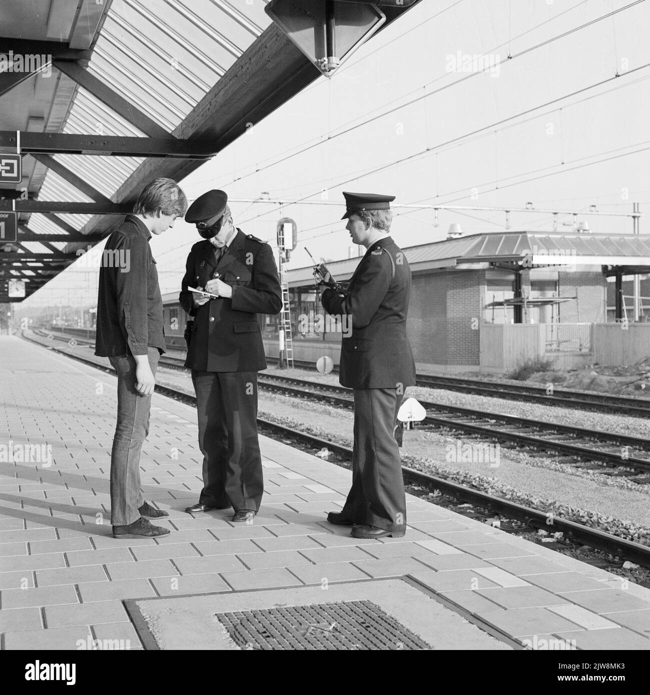 Immagine di due agenti della polizia ferroviaria che verbalizzare un giovane sulla piattaforma della stazione N.S. Ede-Wageningen a Ede. Foto Stock