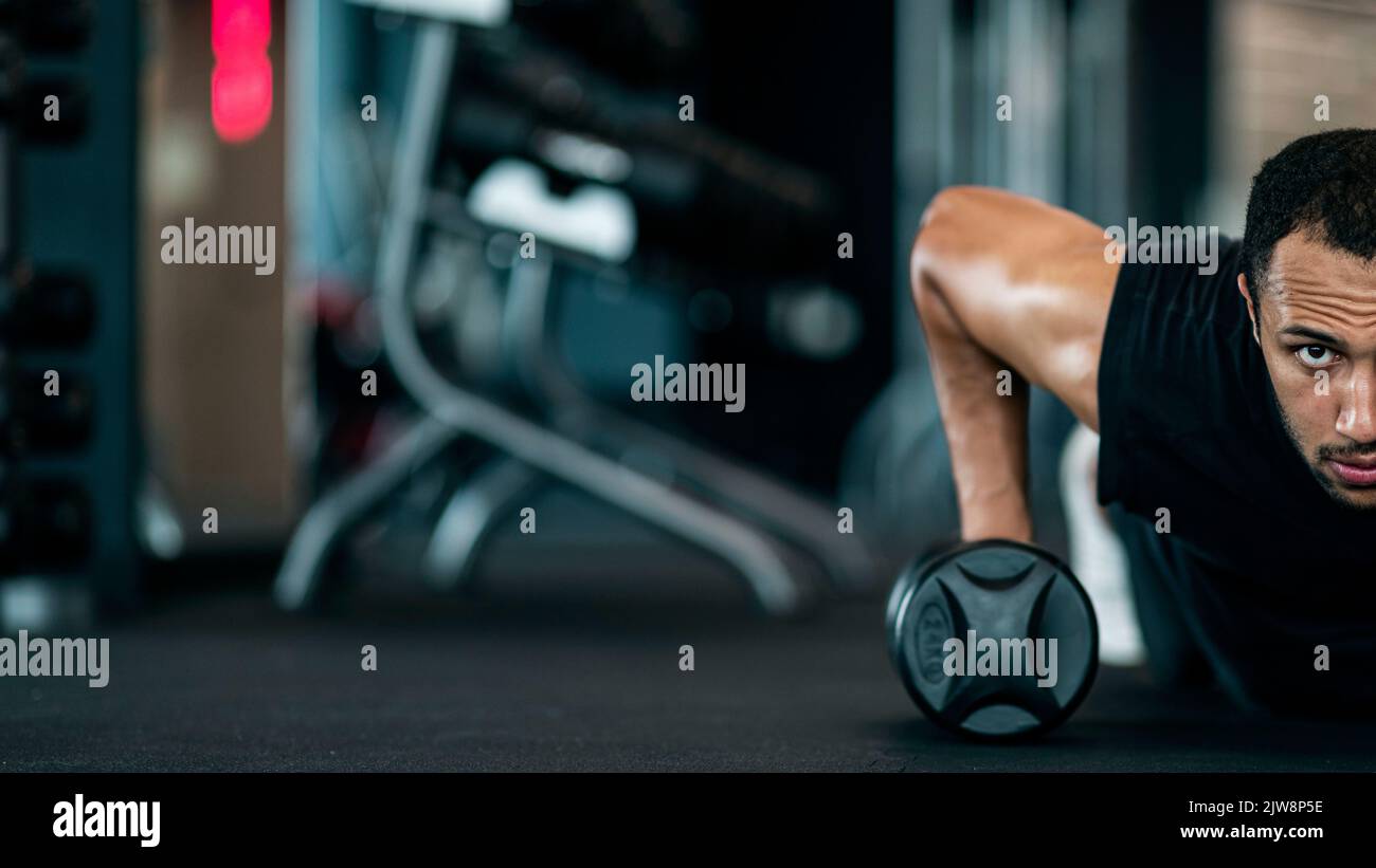 Mezzo ritratto di un uomo nero atletico motivato che fa un esercizio Push-Up con Dumbbell Foto Stock