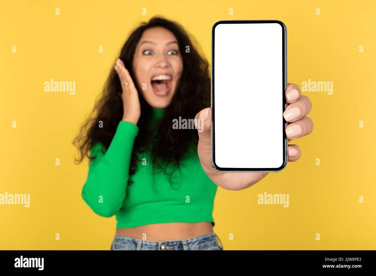 Emotiva Signora araba che mostra lo schermo del telefono su sfondo giallo studio Foto Stock