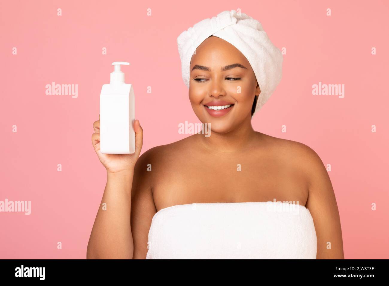 Felice donna oversize nero che tiene la bottiglia cosmetic sopra lo sfondo rosa Foto Stock