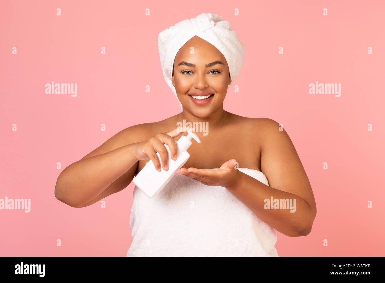 Donna Africana americana sovrappeso che tiene la bottiglia cosmetic sopra lo sfondo rosa Foto Stock