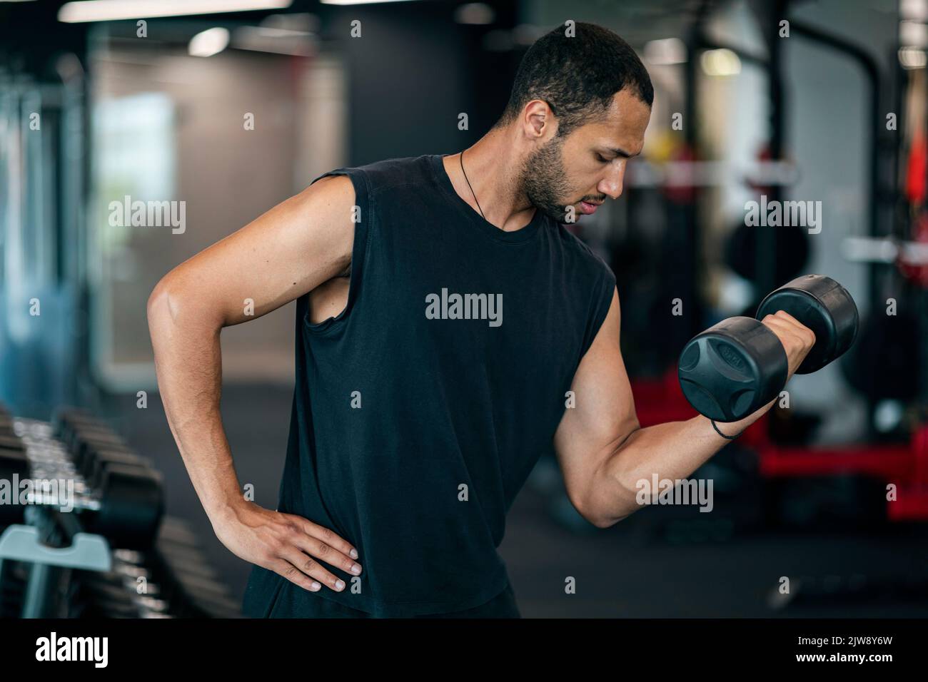 Bel giovane afro-americano che fa allenamento di bodybuilding con manubri in palestra Foto Stock