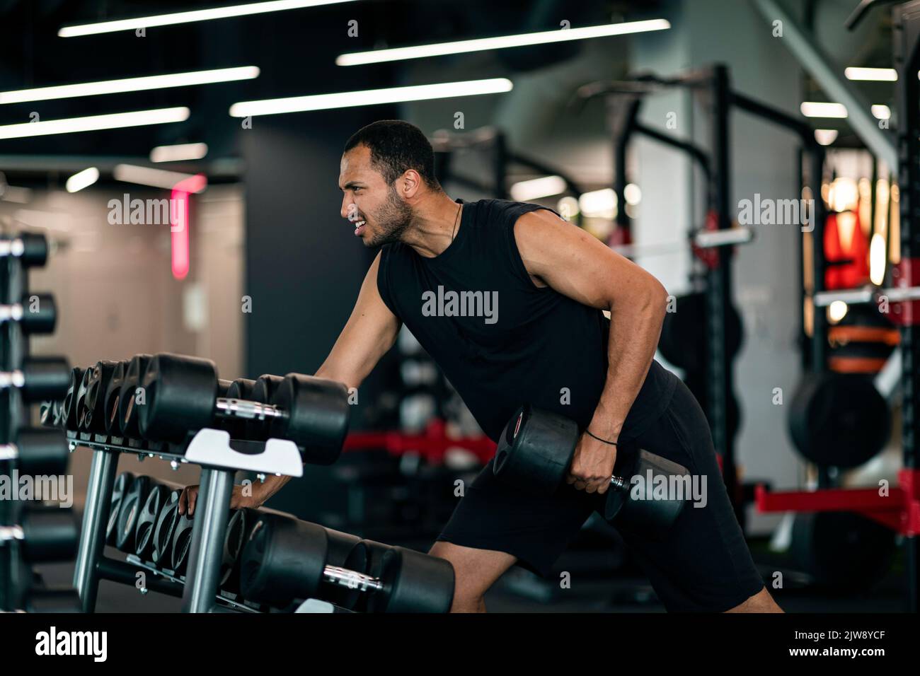Motivata giovane atleta nero maschio esercizio con la Dumbbell alla palestra moderna Foto Stock
