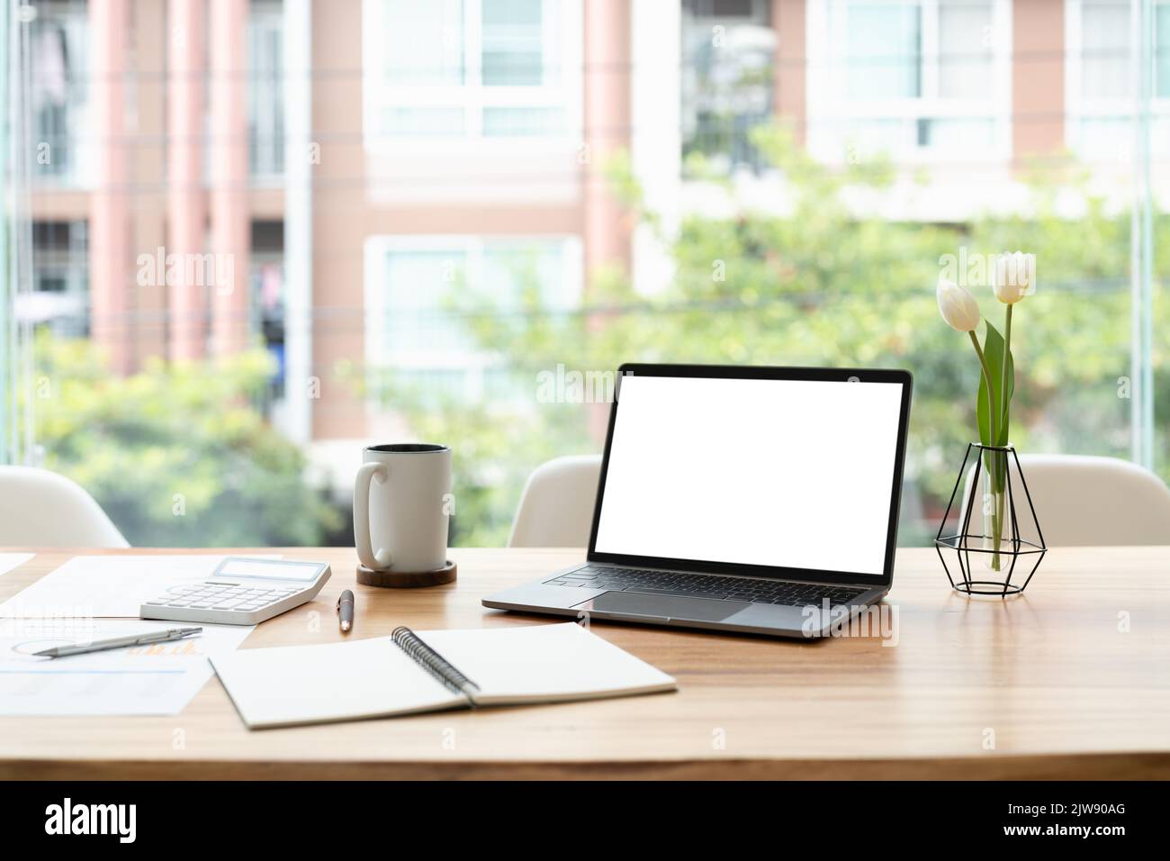 Moderna scrivania da ufficio con computer portatile aperto, schermo bianco, report finanziari e marketing, calcolatrice e forniture. Foto Stock
