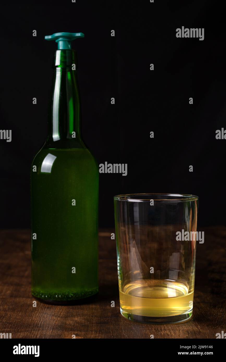 Bottiglia di sidro con un versatore accanto ad un bicchiere con un po' di sidro, con la quantità normale che il sidro viene solitamente servito. Foto Stock