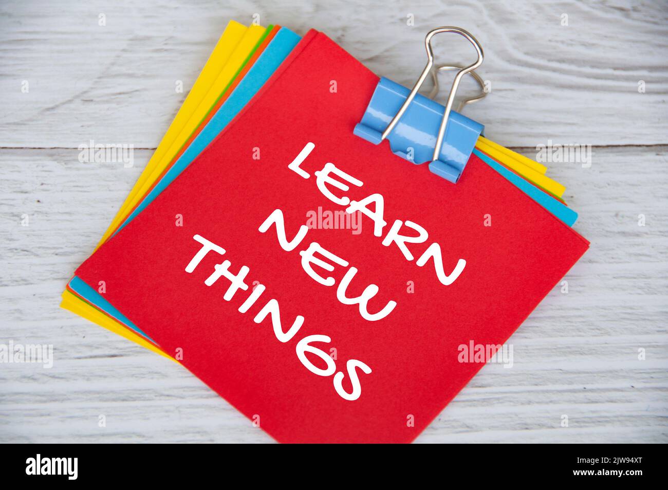 Impari il testo nuovo delle cose sul blocco note rosso su sfondo bianco di legno. Concetto di apprendimento. Foto Stock