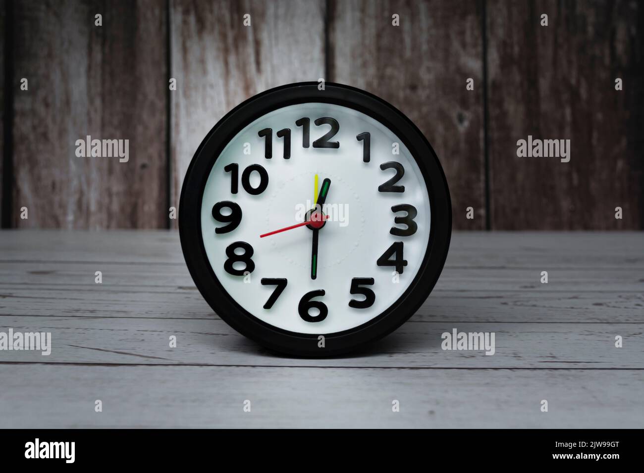 Sveglia nera isolata sulla scrivania in legno. L'orologio è stato impostato a metà e a dodici. Concetto di scadenza. Foto Stock