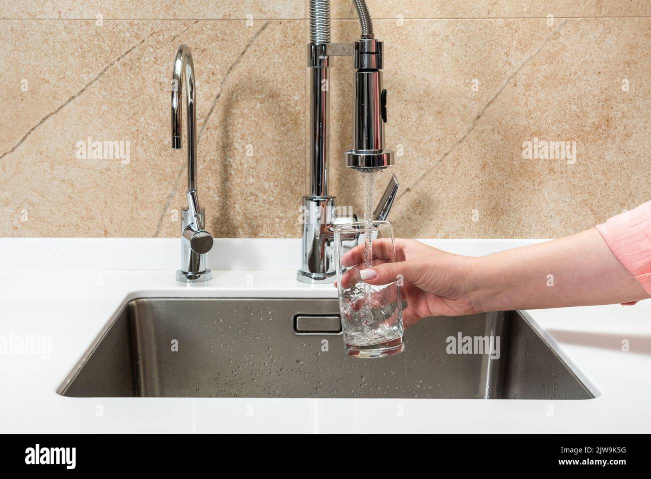 Qualcuno aspira l'acqua dal rubinetto in cucina in un bicchiere Foto Stock