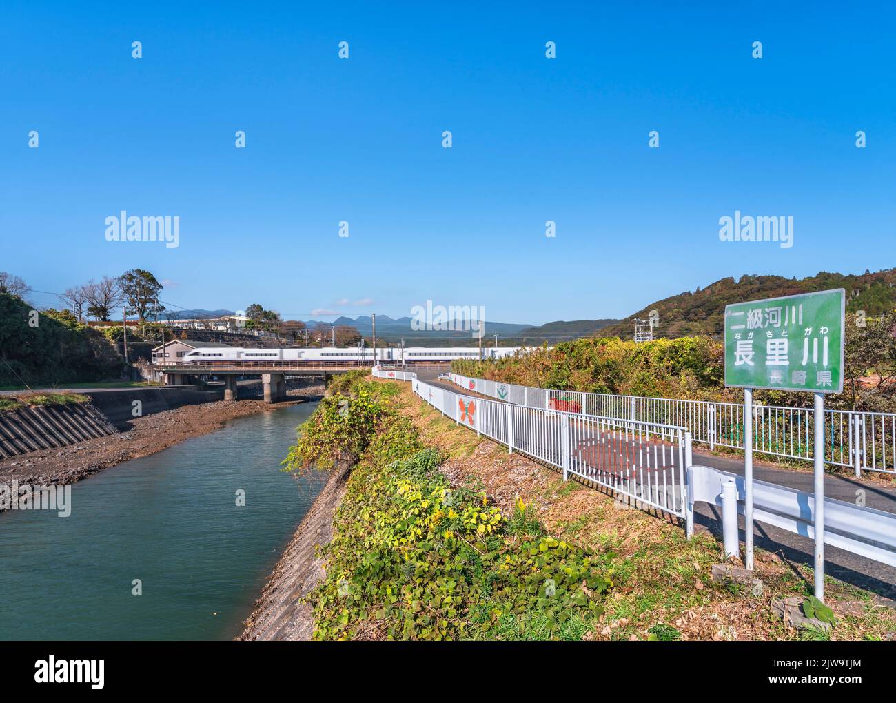 kyushu, giappone - dicembre 10 2021: Il fiume Nagasato attraversato da un treno sulla linea principale di Nagasaki a parte un percorso adornato con illustrazioni di insetti e. Foto Stock