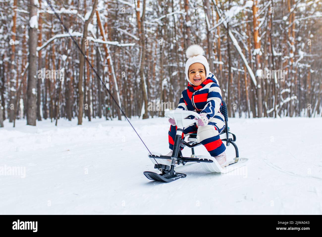 bambina che gioca nella nevosa giornata invernale nel parco in slitta giù per la collina Foto Stock