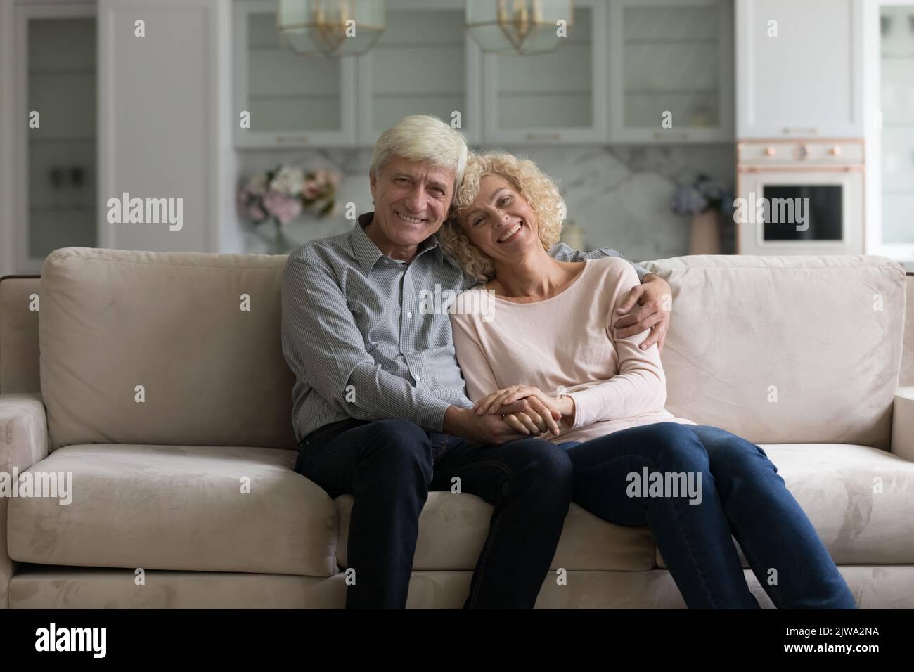 Felice coppia sposata cute anziana seduta sul divano di casa, abbracciando Foto Stock