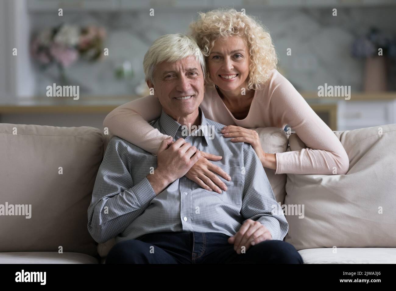 Felice bella moglie abbracciando marito anziano da dietro con amore Foto Stock