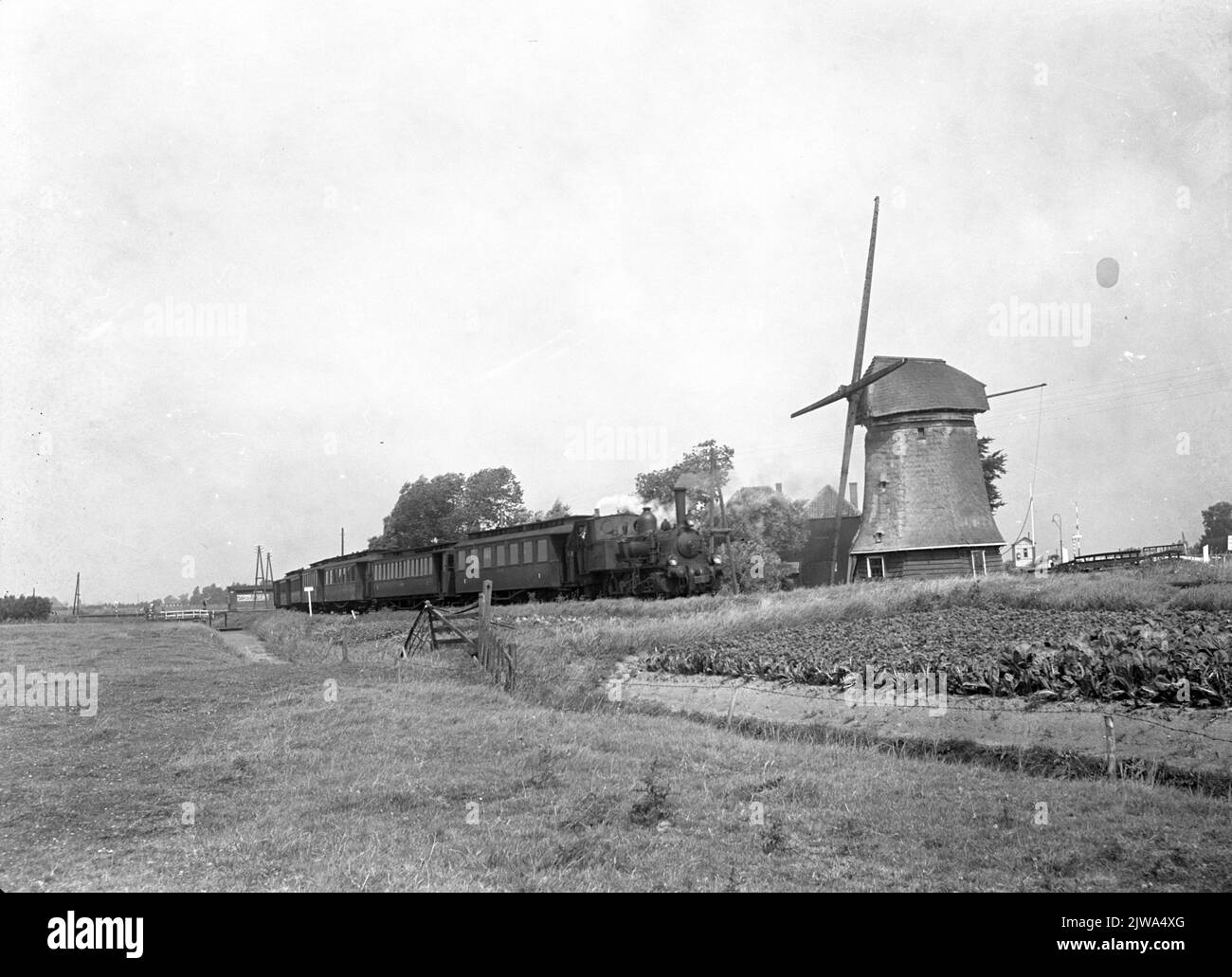 Immagine della locomotiva a vapore n° 7742 (serie 7700, bello) della N.S. Con carrozze in un paesaggio con mulino a Koedijk. Foto Stock