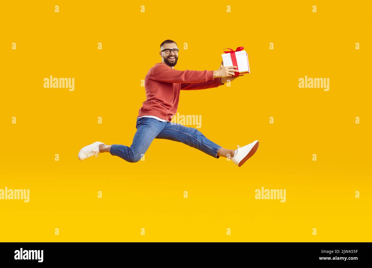 Uomo felice tenendo la scatola del regalo e saltando in aria isolato su sfondo giallo arancione Foto Stock