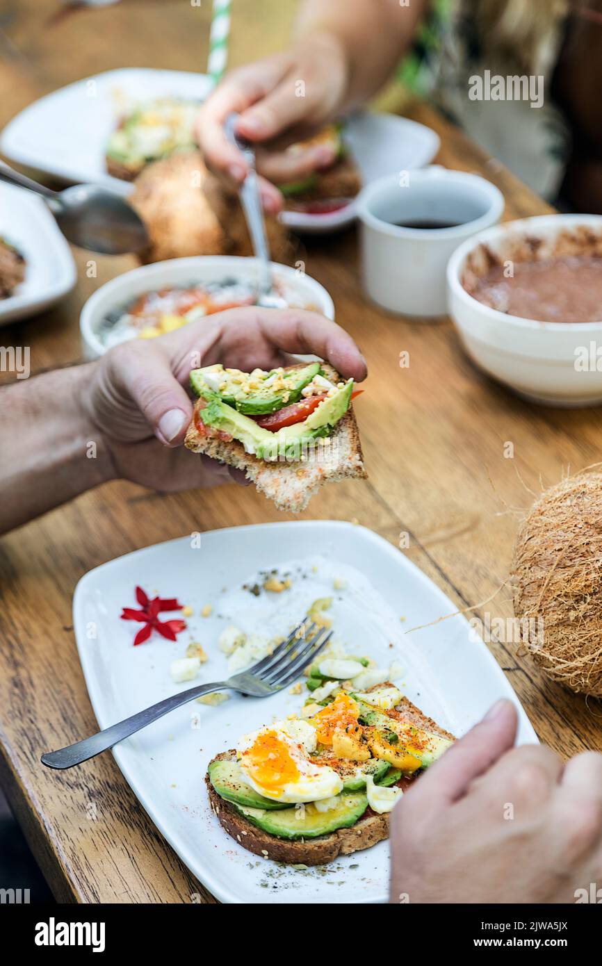 Gli amici potranno gustare una colazione vegetariana con pane tostato, uova strapazzate, cocco e avocado. Godendo la compagnia di amici e cibo. Atmosfera estiva Foto Stock
